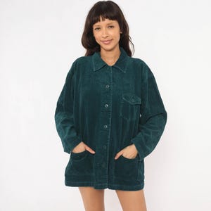 May include: A dark teal corduroy jacket featuring a collared neckline, a button-down front, long sleeves, and two large patch pockets at the lower front. The garment has a textured, ribbed fabric finish and a single chest pocket on the left side.