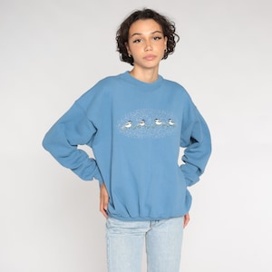 May include: A blue sweatshirt featuring a graphic of five birds on a branch with a snowy background.