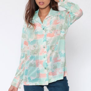 Puede incluir: Una camisa de manga larga con un estampado abstracto en tonos pastel de azul, rosa y verde. La camisa tiene cuello y pu&ntilde;os abotonados. La modelo lleva vaqueros azules.