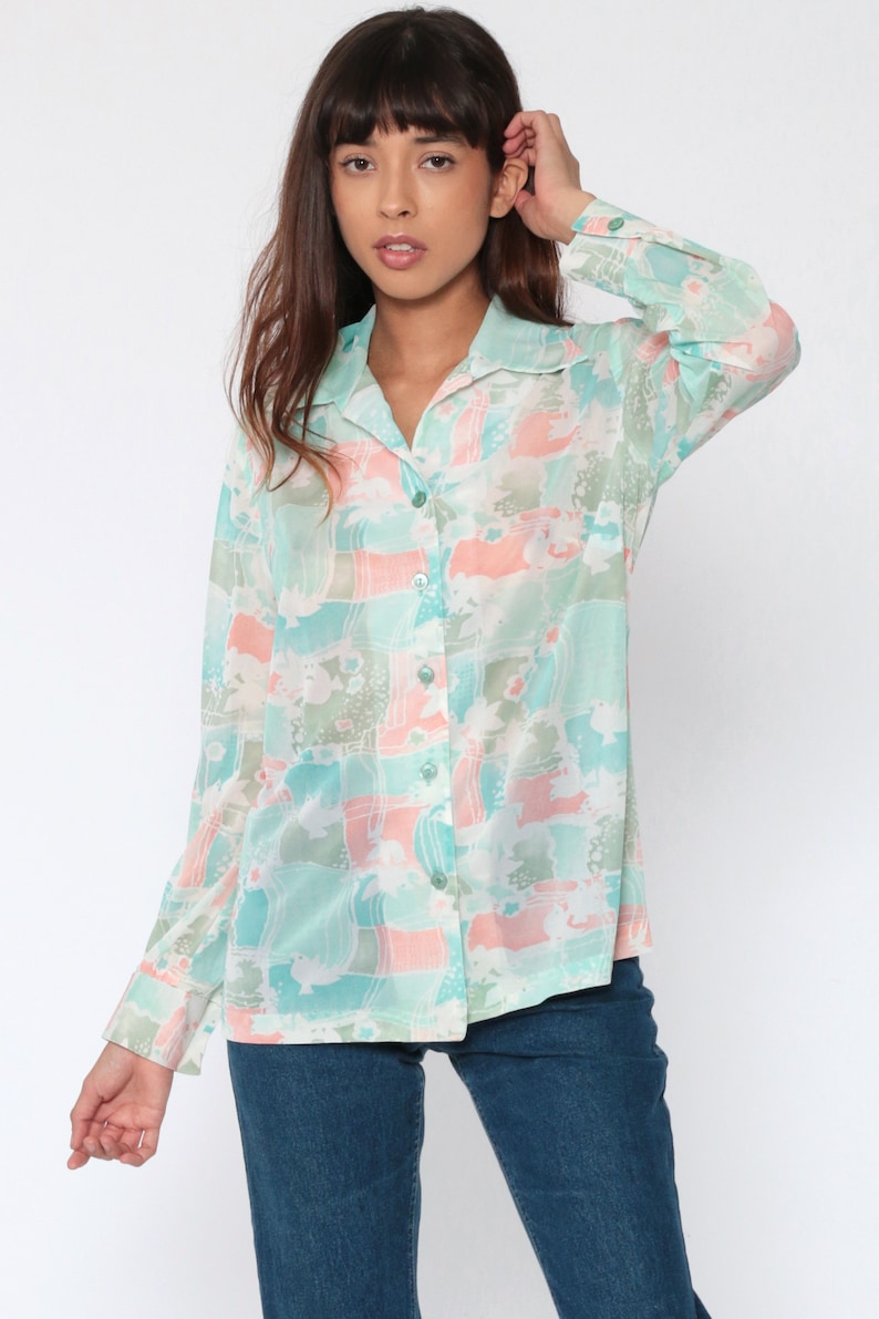 Puede incluir: Una camisa de manga larga con un estampado abstracto en tonos pastel de azul, rosa y verde. La camisa tiene cuello y pu&ntilde;os abotonados. La modelo lleva vaqueros azules.