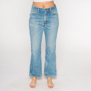 May include: Light blue denim jeans with a slight flare at the hem. The jeans have a button and zip closure, front and back pockets, and show some wear. A classic style.