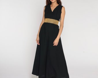 Puede incluir: Un vestido maxi negro con un cinturón dorado. El vestido tiene un escote en V y es sin mangas.