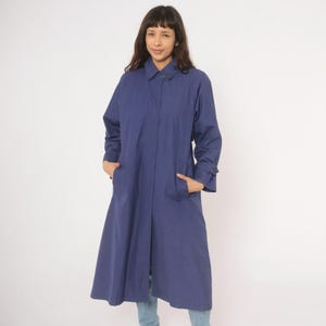 May include: A long, navy blue coat with a collared neckline and button closure. The coat features long sleeves with buttoned cuffs and two front pockets. The coat is knee-length and made of a smooth fabric.