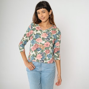 May include: A white, floral print, 3/4 sleeve button-up shirt with pink, blue, and green flowers.