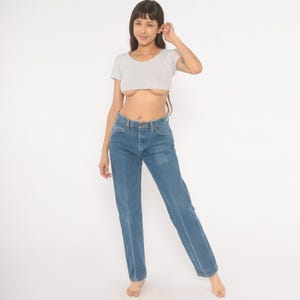 May include: A light gray crop top and blue jeans. The short-sleeved top has a scoop neck. The jeans are a medium wash with a straight leg and a button and zipper closure.