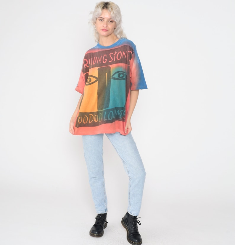 May include: A tie-dye t-shirt with a colorful graphic of the Rolling Stones logo and the text "Voodoo Lounge".