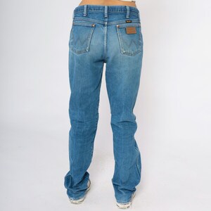 May include: Light blue denim jeans with a classic fit, featuring a brown leather patch on the back pocket. The jeans have a traditional five-pocket design and a faded wash for a vintage look.