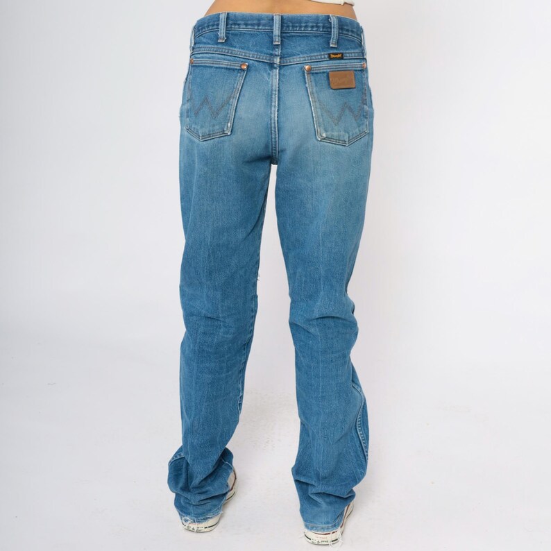 May include: Light blue denim jeans with a classic fit, featuring a brown leather patch on the back pocket. The jeans have a traditional five-pocket design and a faded wash for a vintage look.