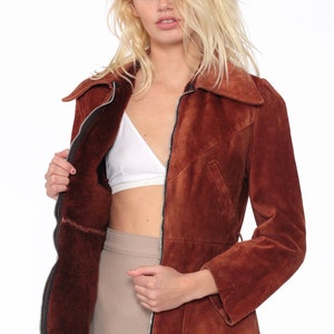 May include: A brown suede jacket with a zipper closure and a fur-lined interior. The jacket has a collar and long sleeves.