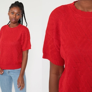 May include: Red short-sleeved sweater with a diamond pattern knit. The sweater has a crew neck.