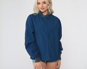 May include: A blue zip-up jacket with a stand-up collar. The jacket has long sleeves and a zipper closure.