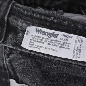 May include: Close-up of black Wrangler jeans. The label reads "Wrangler 13MWZWK 34 x 30". The jeans are made of 100% cotton and made in Mexico of US fabric. The care instructions are also visible on the label.