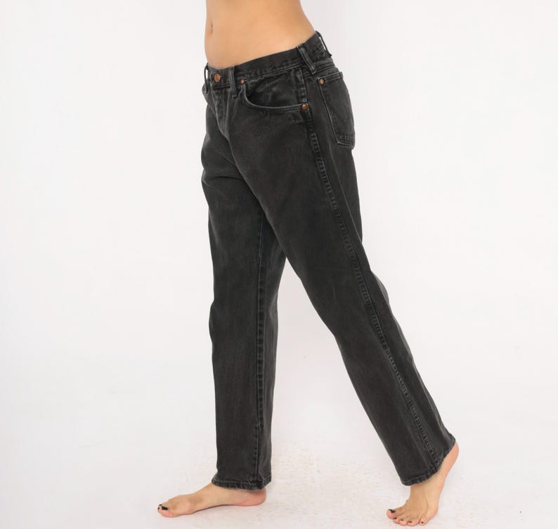 May include: Black denim jeans with a classic five-pocket design. The jeans have a straight leg cut and a faded appearance. The dark wash denim features copper-colored rivets and a button closure. The jeans are worn casually.