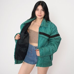 May include: A teal blue puffer jacket with black stripes on the sleeves and a black zipper. The jacket is unzipped and the lining is black.