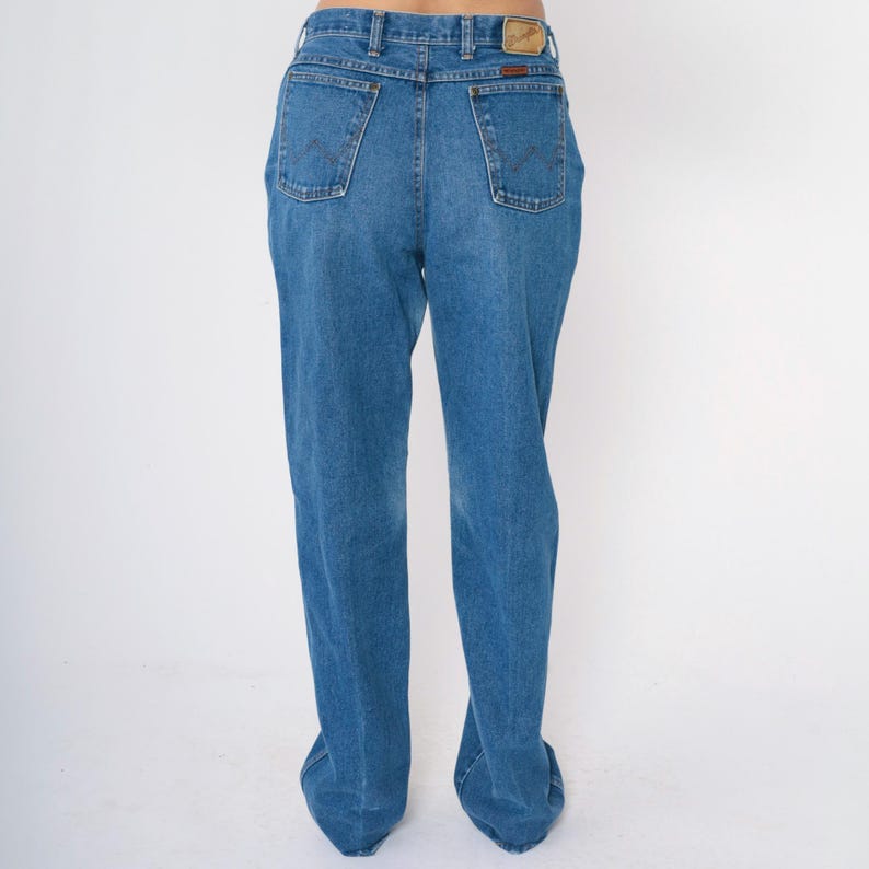 May include: A pair of blue denim jeans with a straight leg fit. The jeans have a classic five-pocket style and a brown leather patch on the back waistband.