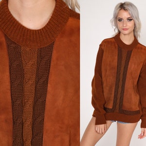 May include: A brown suede and knit sweater with a cable knit design. The sweater has a crew neck and long sleeves.