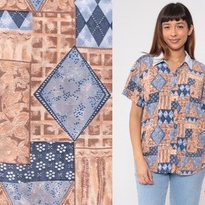 Può includere: Una camicia a maniche corte con bottoni e un design a patchwork con forme geometriche e motivi floreali in tonalità di marrone e blu.