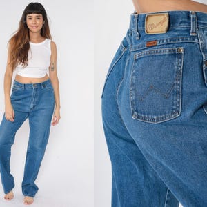 May include: A pair of blue denim jeans with a high waist and a wide leg. The jeans have a Wrangler logo on the back pocket.