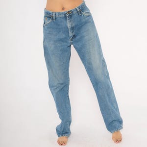 Pu&ograve; includere: Jeans di denim blu chiaro con un classico design a cinque tasche. I jeans hanno un taglio dritto e una chiusura con bottone e cerniera. Il denim ha un lavaggio sbiadito, che gli conferisce un aspetto vintage. I jeans sono indossati da una persona.