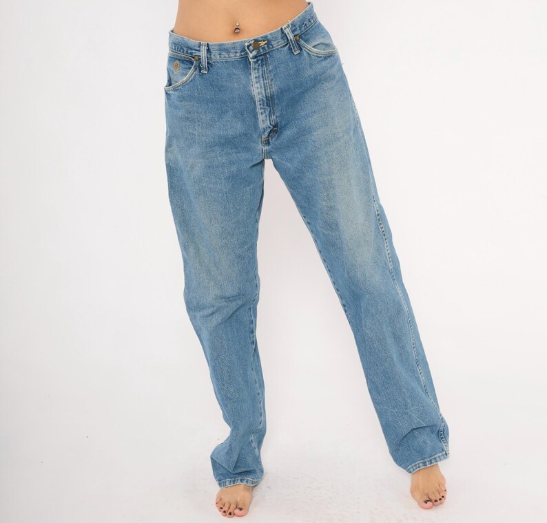 Pu&ograve; includere: Jeans di denim blu chiaro con un classico design a cinque tasche. I jeans hanno un taglio dritto e una chiusura con bottone e cerniera. Il denim ha un lavaggio sbiadito, che gli conferisce un aspetto vintage. I jeans sono indossati da una persona.