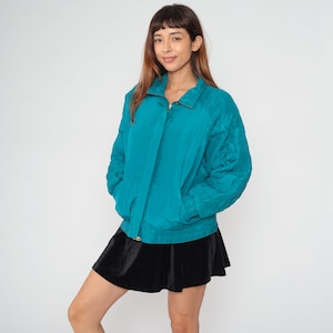 May include: A teal blue zip-up jacket with a stand-up collar. The jacket has a quilted design on the sleeves and a smooth fabric on the body.