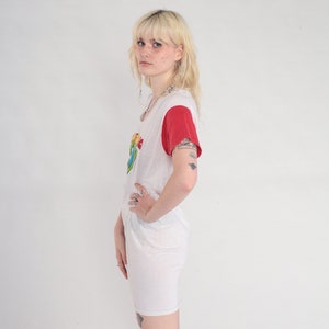 K&ouml;nnte beinhalten: Ein wei&szlig;es T-Shirt-Kleid mit roten &Auml;rmeln und einem bunten Grafikdruck. Das Kleid hat einen runden Ausschnitt und eine lockere Passform.