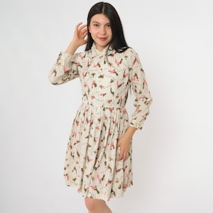Può includere: Un vestito color crema con scollo a camicia e maniche lunghe. L'abito presenta un motivo a righe verticali con piccole illustrazioni ripetute in rosso e verde. L'abito ha un corpetto aderente e una gonna svasata.