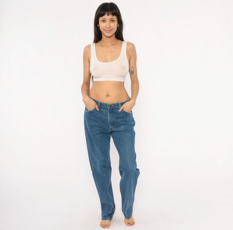 May include: A light-colored, scoop-neck crop top and blue jeans. The jeans have a classic five-pocket design and a relaxed fit. The model is standing in front of a white background.