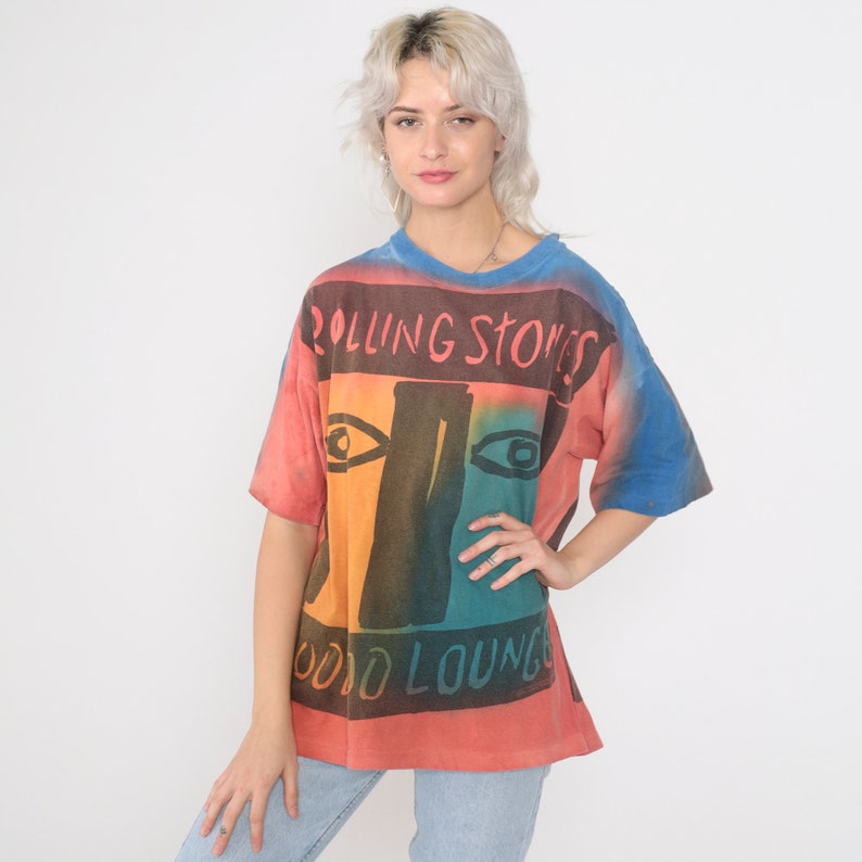 May include: A tie-dye t-shirt with a colorful graphic of a face and the text "Rolling Stones Mood Lounge".