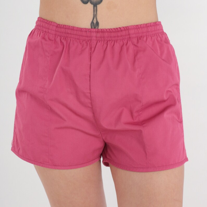 May include: Pink shorts with an elasticated waistband. The shorts are made from a smooth, lightweight material and have a simple, classic design. The shorts are a vibrant shade of pink.
