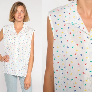 May include: White sleeveless button-down shirt with a colorful teardrop pattern. The shirt has a collar and buttons down the front. The teardrops are red, yellow, blue, and green.