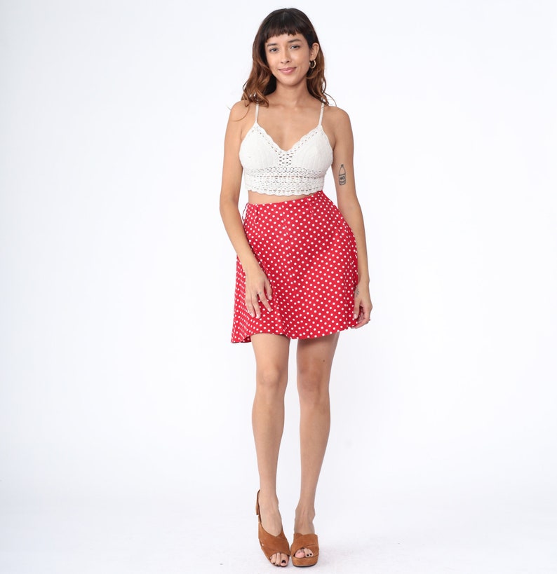 Peut inclure: Une jupe mini &agrave; pois rouges avec un haut en crochet blanc. La jupe a une fermeture &agrave; boutons et une silhouette &eacute;vas&eacute;e.