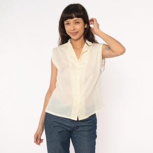 May include: A pale yellow sleeveless shirt with a collared neckline and button-down front. The shirt appears to be made from a lightweight fabric. The garment is suitable for warmer weather and has a slightly textured appearance.