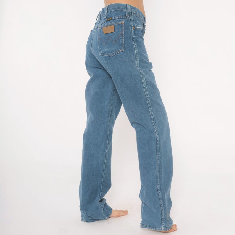 May include: Light blue denim jeans with a classic straight leg fit. The jeans feature a brown leather patch on the back pocket with a brand logo. The jeans have a traditional five-pocket design and a button and zipper closure.