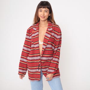 Könnte beinhalten: Ein roter Blazer mit einem Streifenmuster in Schwarz, Gelb und Grau. Der Blazer hat ein Revers und lange Ärmel. Das Model trägt eine blaue Jeans.
