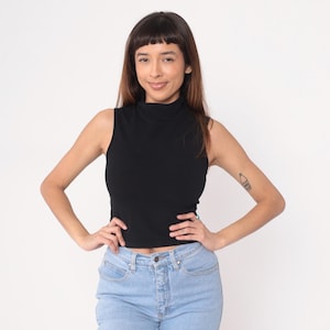 Peut inclure: Un haut noir sans manches à col montant et un jean en denim bleu clair. Le haut est de couleur unie et semble être fait d'une matière douce et extensible. Le jean a une conception classique à cinq poches.