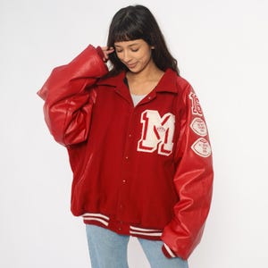 May include: Red varsity jacket with white accents and leather sleeves. Features a large white "M" patch on the chest and patches on the right sleeve. The jacket has a button-up front and a classic collar.
