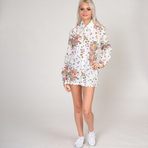 May include: A white long-sleeved shirt with a geometric pattern in shades of pink, yellow, and blue. The shirt has a collared neckline and button closure.
