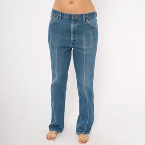 Peut inclure: Jean bleu en denim avec une conception classique &agrave; cinq poches. Le jean a une coupe droite et une apparence d&eacute;lav&eacute;e. L'avant comporte une fermeture &agrave; bouton et &agrave; glissi&egrave;re. Le jean est de couleur moyenne et semble vintage.