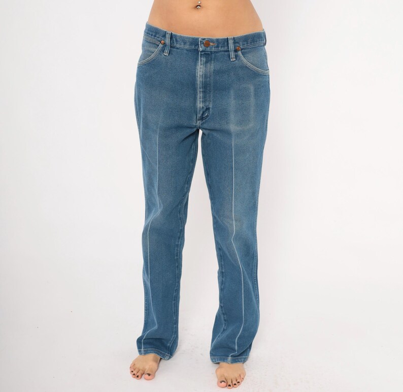 Peut inclure: Jean bleu en denim avec une conception classique &agrave; cinq poches. Le jean a une coupe droite et une apparence d&eacute;lav&eacute;e. L'avant comporte une fermeture &agrave; bouton et &agrave; glissi&egrave;re. Le jean est de couleur moyenne et semble vintage.