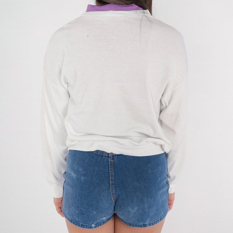 May include: A white long-sleeved shirt with a purple collar and blue denim shorts.