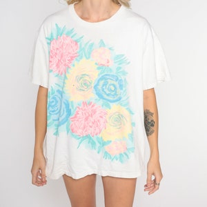 Puede incluir: Camiseta blanca de gran tama&ntilde;o con estampado floral con flores rosas, azules y amarillas sobre fondo blanco.