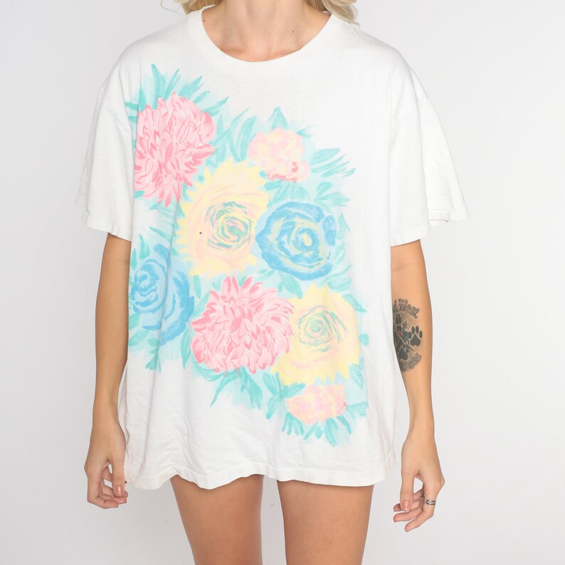 Puede incluir: Camiseta blanca de gran tama&ntilde;o con estampado floral con flores rosas, azules y amarillas sobre fondo blanco.