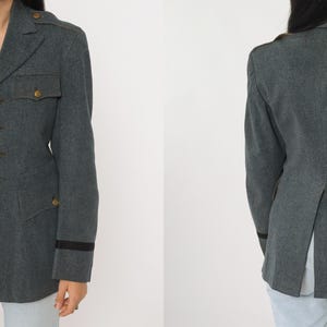 K&ouml;nnte beinhalten: Graue Jacke im Milit&auml;rstil mit goldenen Kn&ouml;pfen und schwarzem Besatz an den &Auml;rmeln. Die Jacke hat eine taillierte Passform mit Taschen und einem Reverskragen. Das Bild zeigt die Vorder- und R&uuml;ckseite der Jacke.