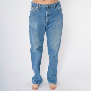 Pu&ograve; includere: Un paio di jeans blu chiaro a gamba dritta. I jeans hanno una chiusura con bottoni e cinque tasche.