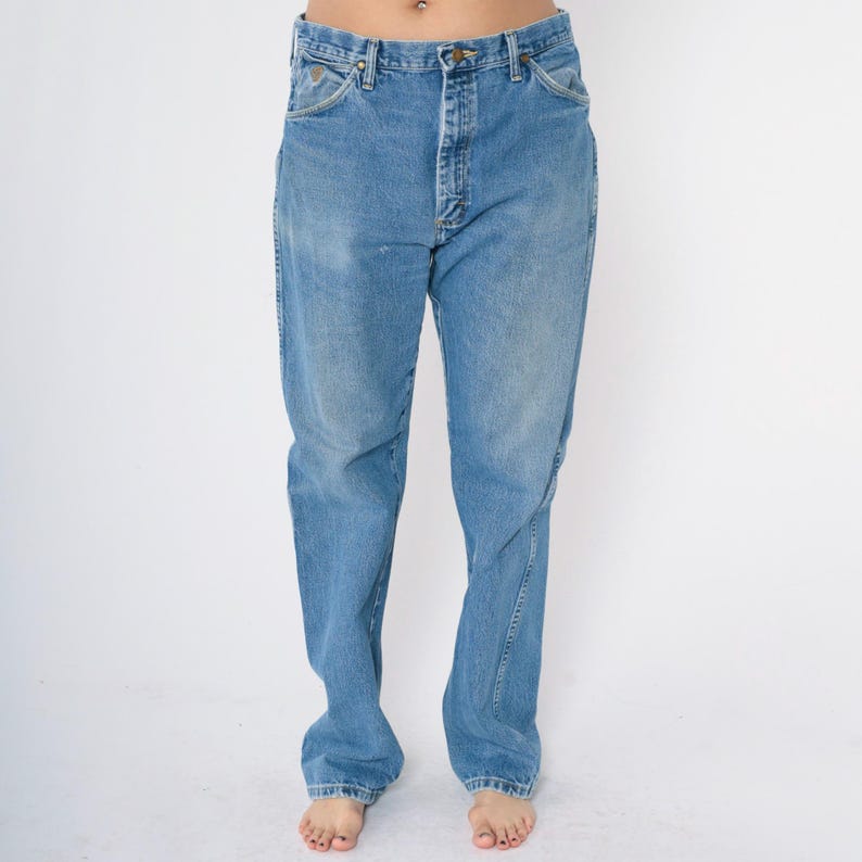Pu&ograve; includere: Un paio di jeans blu chiaro a gamba dritta. I jeans hanno una chiusura con bottoni e cinque tasche.