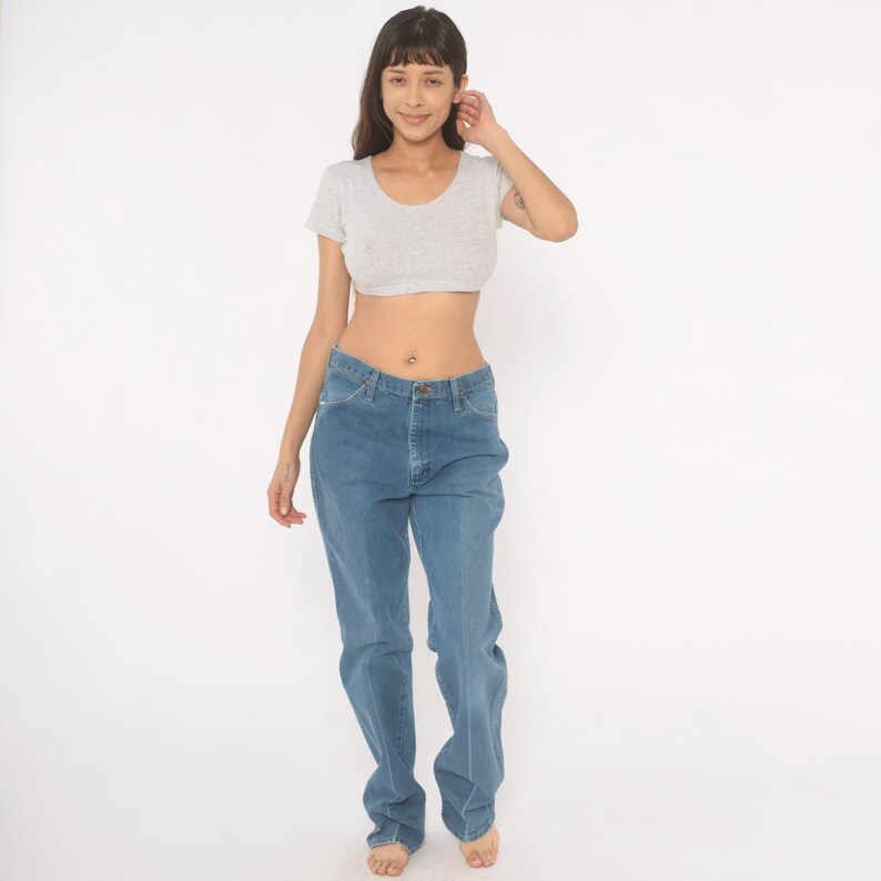 May include: A light gray crop top and blue jeans. The crop top has short sleeves and a scoop neck. The jeans are a medium wash denim with a straight leg. The model is standing in front of a white background.