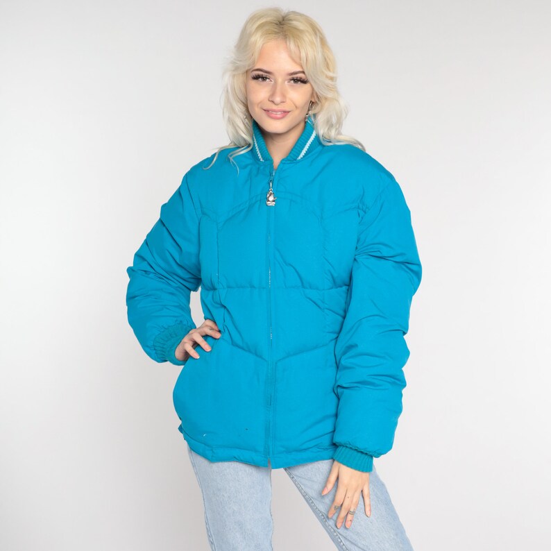 May include: A bright blue puffer jacket with a zipper closure and a white trim around the collar. The jacket has a quilted design and is made of a lightweight material.
