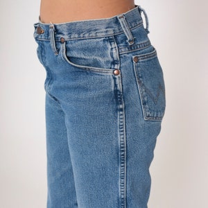 May include: A pair of blue denim jeans with a high waist and a straight leg. The jeans have a classic five-pocket style and a copper button closure.