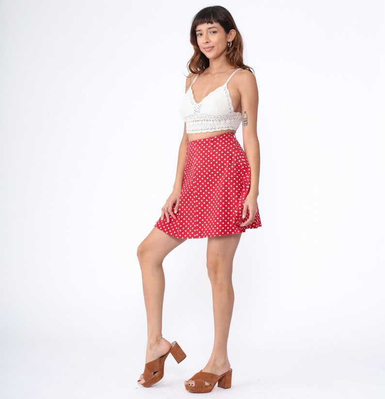 Peut inclure: Une jupe &agrave; pois rouge et blanc avec un haut en crochet blanc. La jupe est trap&egrave;ze et a une taille haute. Le mannequin porte des sandales &agrave; talons marrons.